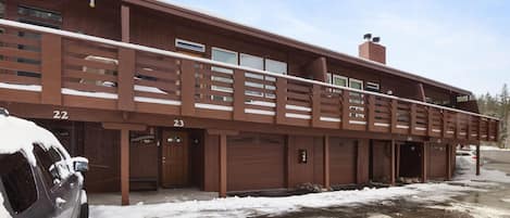 Un immeuble à plusieurs étages, avec des portes de garage numérotées, une allée couverte et un sol recouvert de neige.