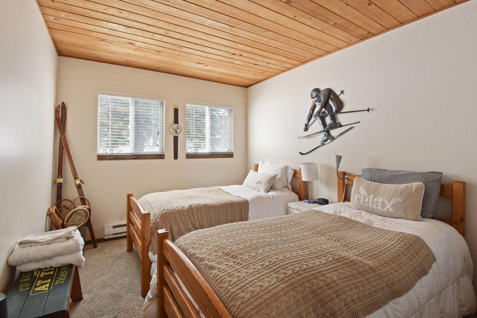 A bedroom with two beds, a wooden ceiling, and a ski-themed wall decoration.