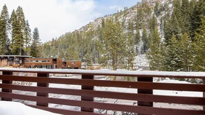A wooden deck with snow-covered ground, a building with a wooden exterior, and a mountainous backdrop. - Alpine Manor Retreat (Olympic Valley)