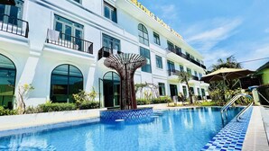 A hotel with a swimming pool, a palm tree sculpture, and a clear blue sky. - D Ng A A Ng Hotel (Phu Quoc)