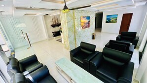 A modern hotel lobby with black leather sofas, a marble column, ceiling fan, and artwork on the walls. - D Ng A A Ng Hotel (Phu Quoc)