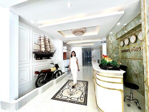 Um saguão de hotel com uma mesa de recepção, um modelo decorativo de navio, uma motocicleta e um piso estampado.