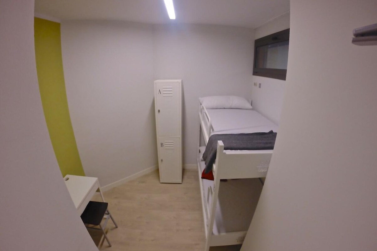 Un petit dortoir composé d’une seule pièce, avec un lit superposé, un bureau et une armoire.