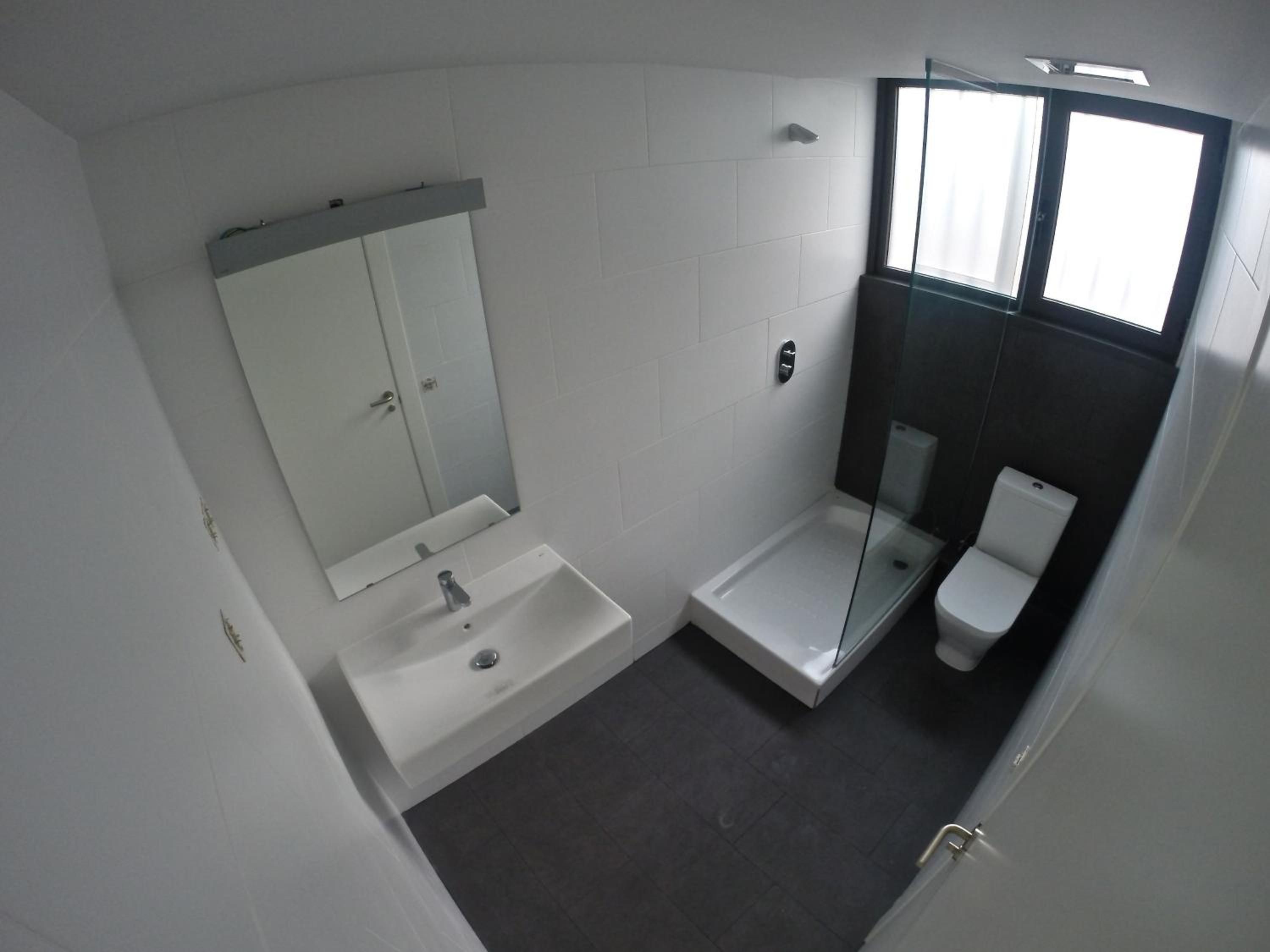 A bathroom with a white sink, a mirror, a glass-enclosed shower, and a toilet.