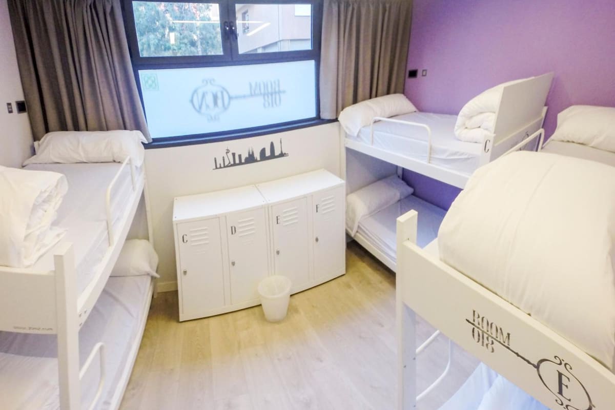 Une chambre d’hôtel avec des lits superposés, une fenêtre avec des rideaux, un petit bureau et un meuble de rangement.