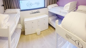 Habitación de hotel con literas, una ventana con cortinas, un escritorio pequeño y un espacio de almacenamiento.