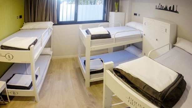 Un dormitorio con literas, una ventana con cortinas, un radiador y el silueta del horizonte urbano en la pared.