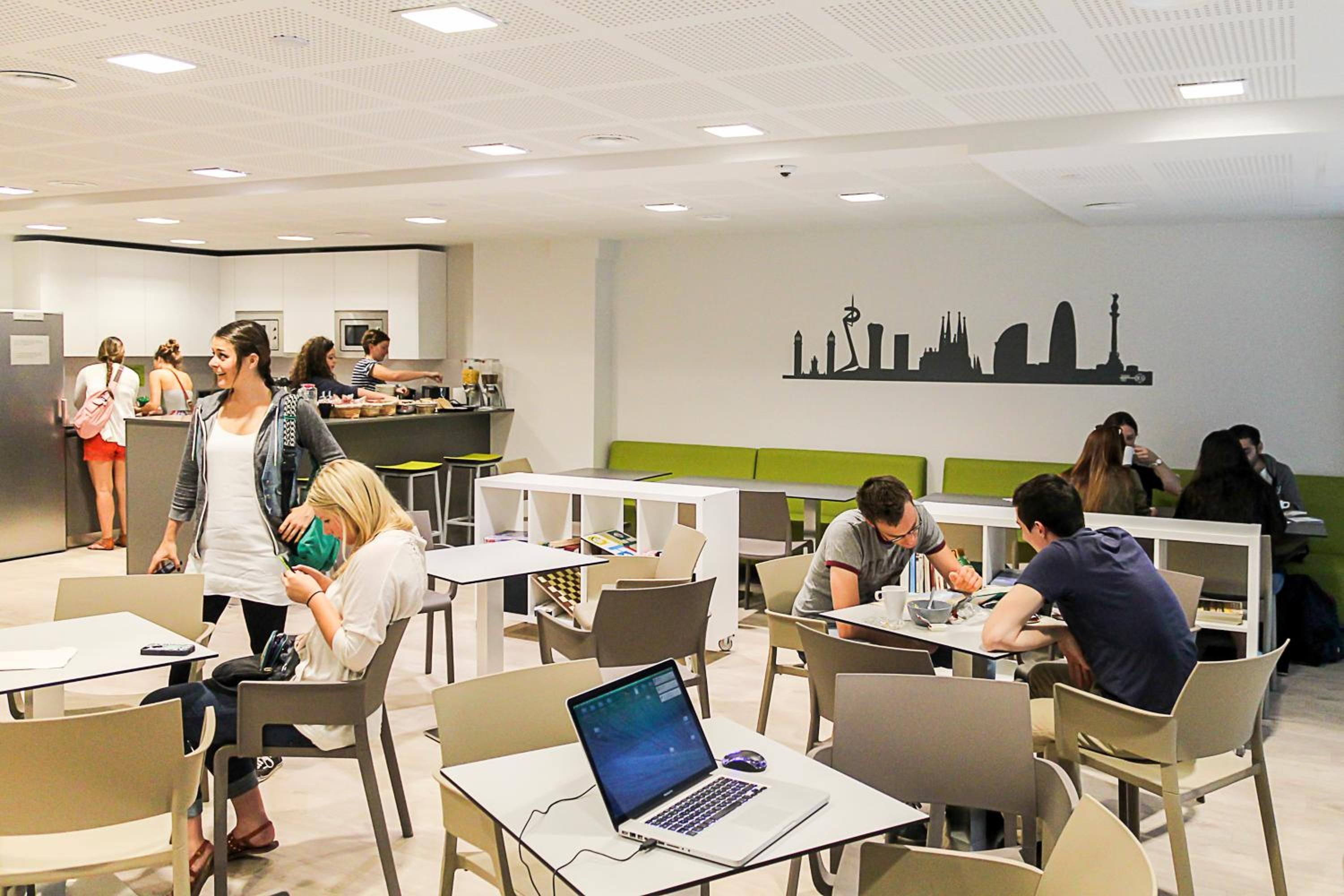 A modern dining area with tables and chairs, a laptop on one table, and a city skyline mural on the wall.