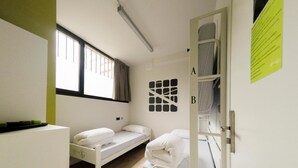 Un dormitorio con dos camas individuales, una ventana y una puerta, y una cama en el otro lado.