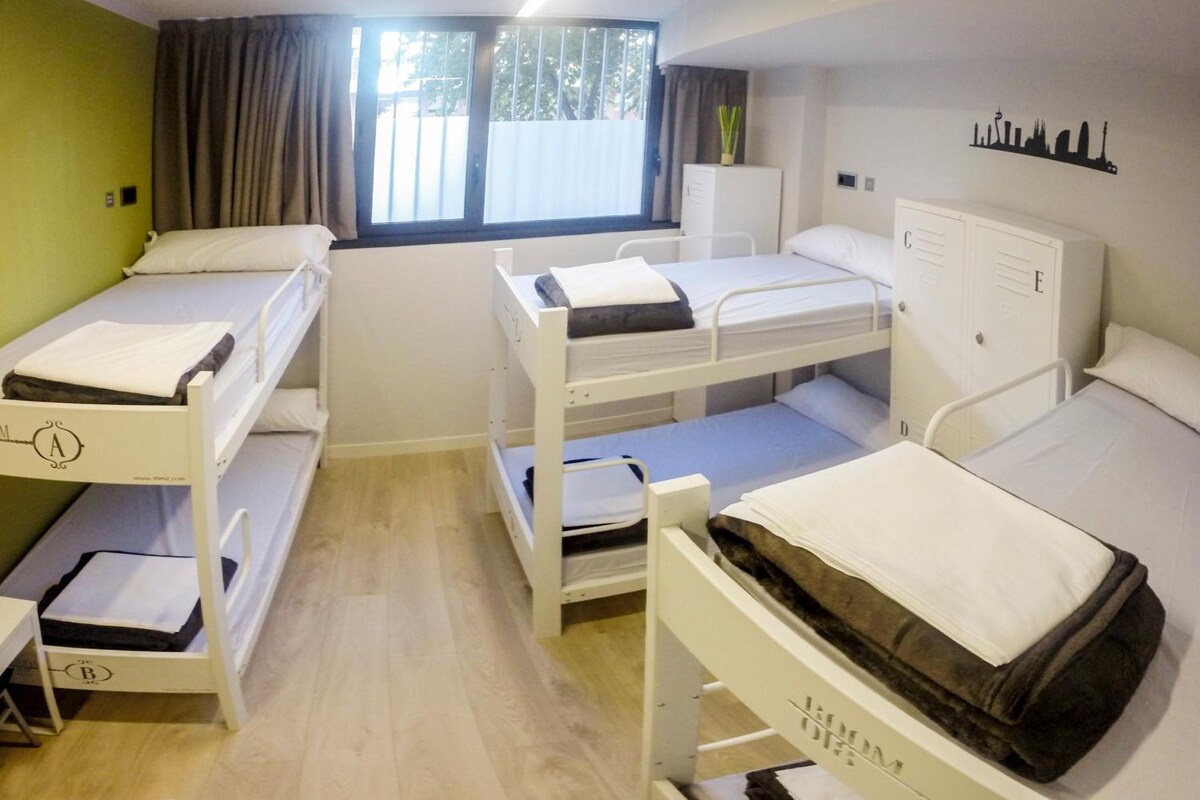 A dormitory room with bunk beds, a window with curtains, a radiator, and a city skyline silhouette on the wall.