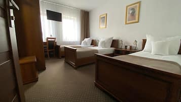 Quarto de hotel com duas camas, uma escrivaninha, uma cadeira, uma televisão e duas imagens emolduradas na parede.