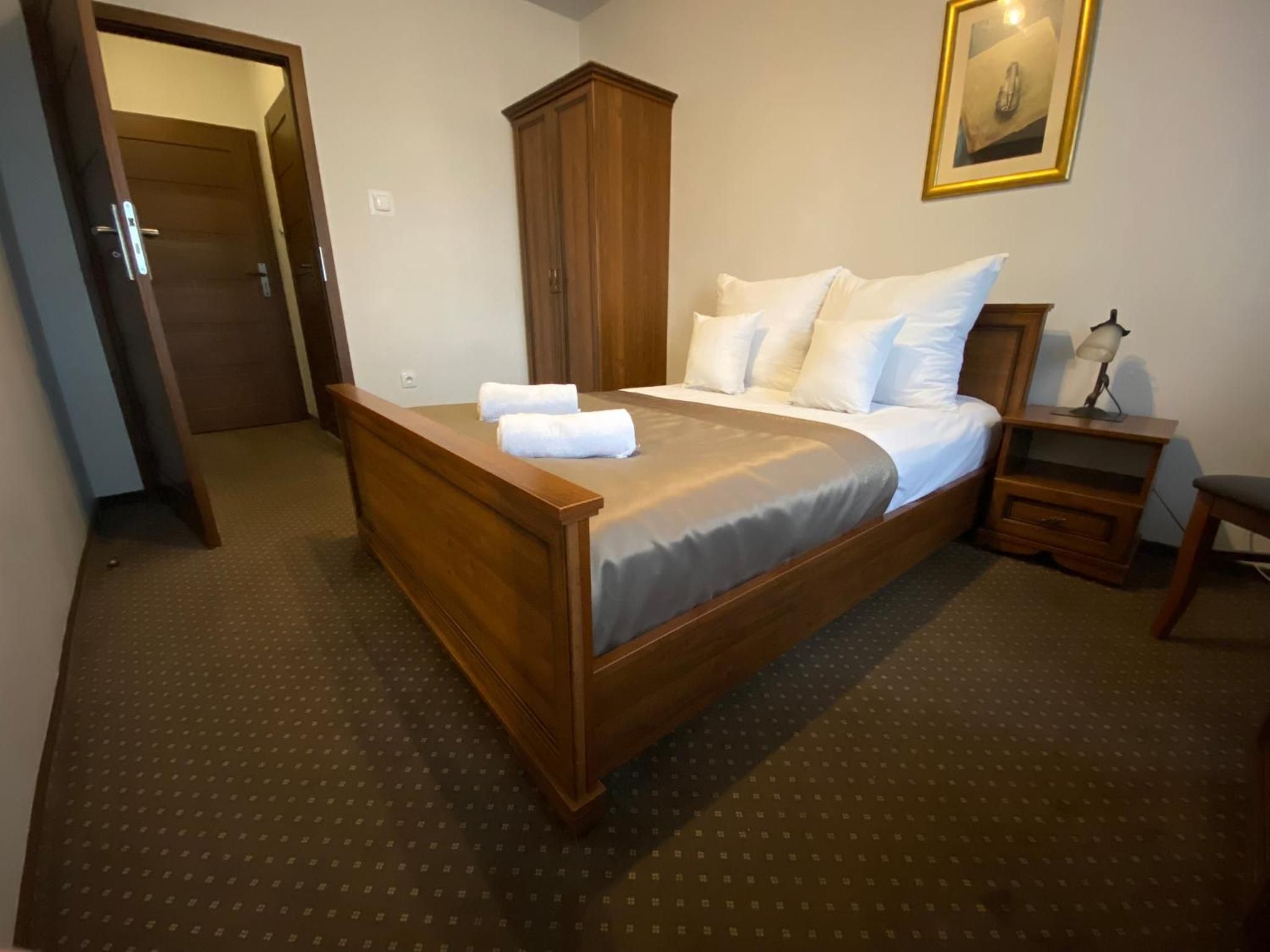 Quarto de hotel com cama de madeira, mesa de cabeceira, escrivaninha e armário.