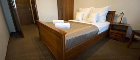 Quarto de hotel com cama de madeira, mesa de cabeceira, escrivaninha e armário.