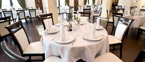 A restaurant with round tables set for dining, featuring white tablecloths and chairs.
