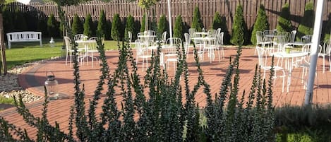 Un patio al aire libre con sillas y mesas de metal blanco, rodeado por una cerca de madera y follaje.