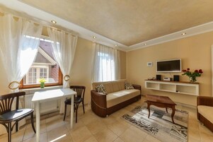 Uma sala de estar mobiliada com sofá, mesa de centro, televisão e uma área de jantar com mesa e cadeiras.