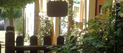 A covered outdoor area with a metal railing, a hanging sign, and potted plants.