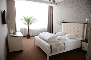 A hotel room with a bed, bedside table, lamp, potted plant, and a desk with a telephone. - Hotel Europa (Baia Mare)