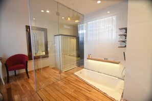 Un baño moderno con cabina de ducha de vidrio, suelo de madera, una silla roja y un estante empotrado con toallas.
