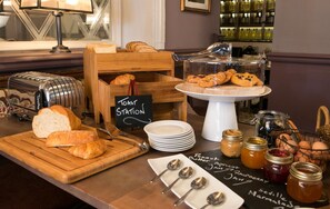 A breakfast buffet with bread, pastries, and condiments. - Dog And Fox (London)