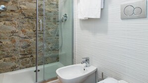 A modern bathroom with a stone wall, a glass-enclosed shower, a bidet, and a toilet with a towel. - Aparthotel Isola (Milan)