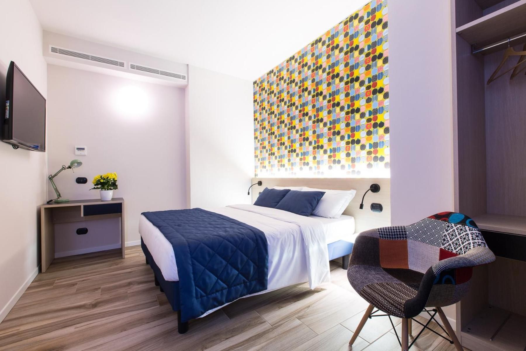 Un dormitorio con cama, mesita de noche, lámpara y una llamativa obra de arte en la pared.