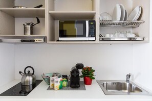 A kitchen with a microwave, kettle, cereal boxes, a coffee maker, and a sink. - Aparthotel Isola (Milan)