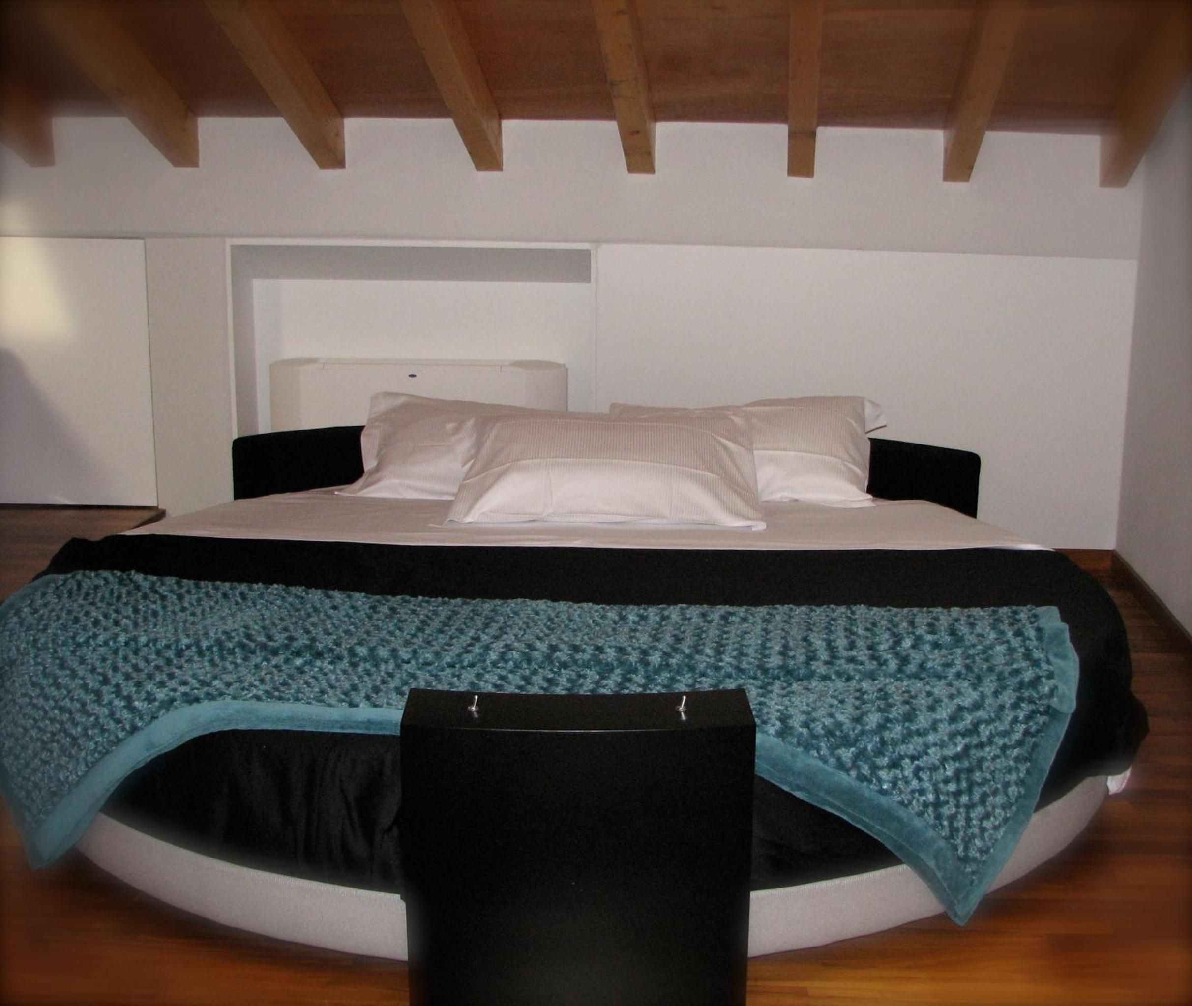 A circular bed with a black headboard, white bedding, and a teal throw blanket.