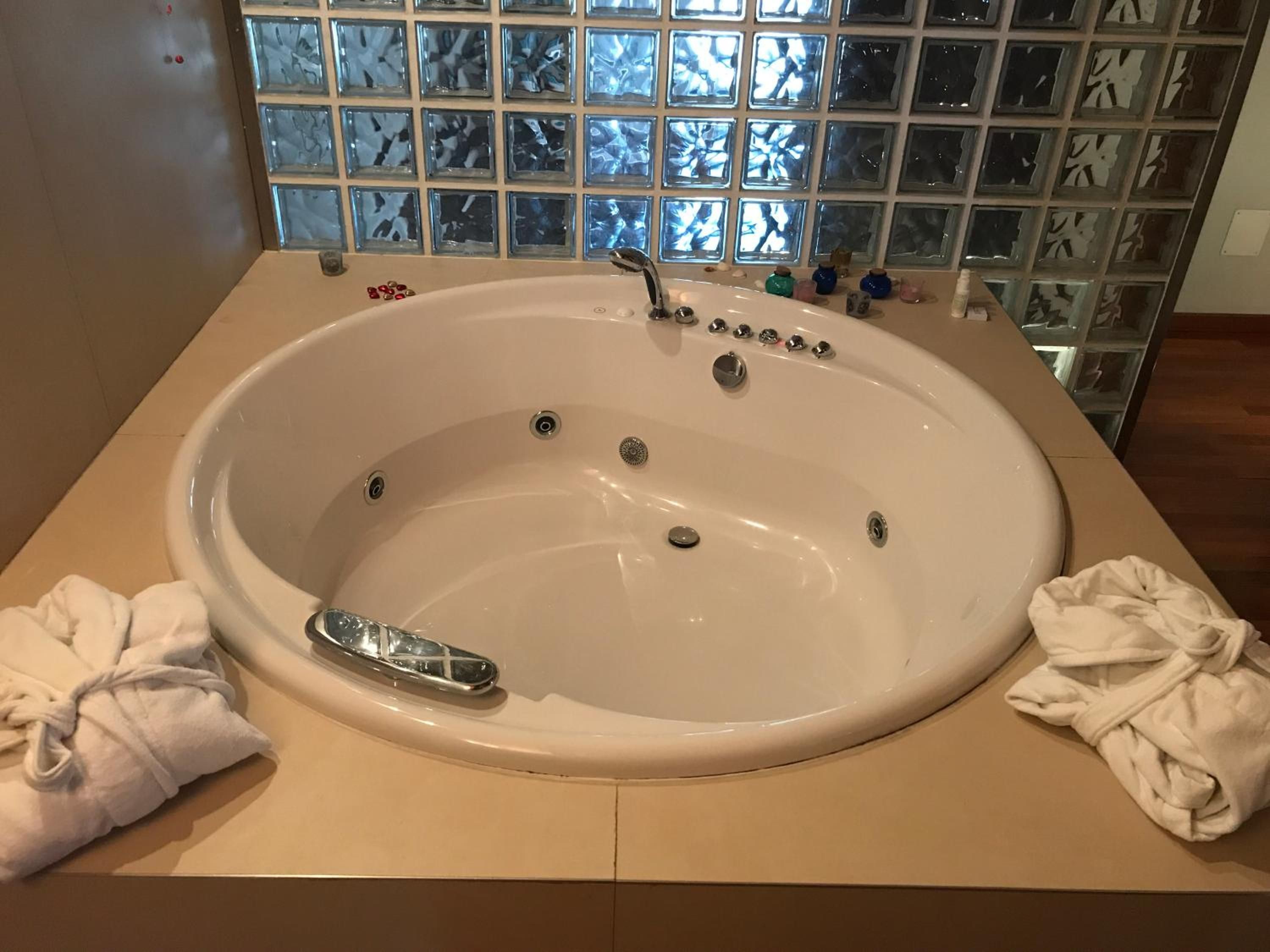 A large oval bathtub with a faucet and multiple controls, set against a tiled wall with a reflective pattern.