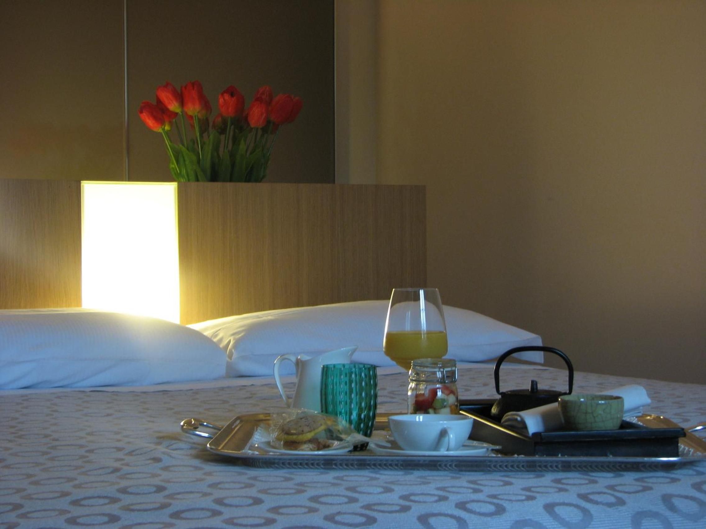 Un vassoio colazione ordinato su un letto, con un vaso di tulipani rossi sullo sfondo.