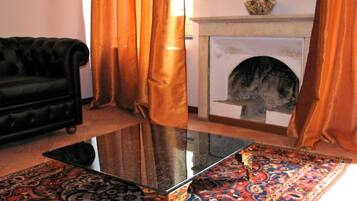 Un soggiorno con un divano nero, un tavolino in vetro, un tappeto decorato, un camino e tende arancioni.