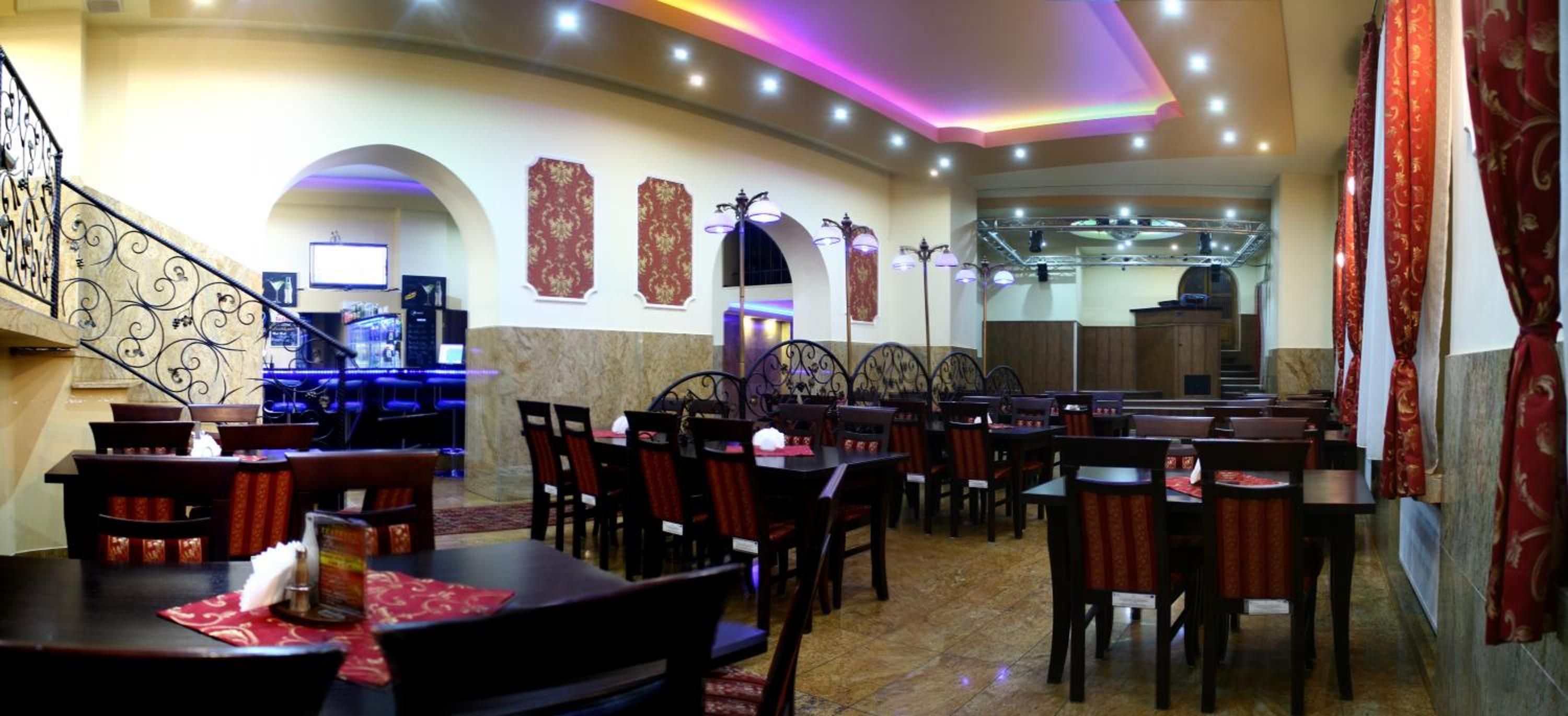 A restaurant with multiple tables and chairs, a staircase, and decorative wall panels.