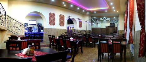 A restaurant with multiple tables and chairs, a staircase, and decorative wall panels.
