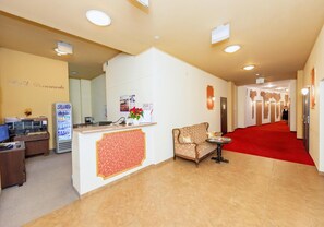 A hotel reception area with a reception desk, a seating area, a red carpet, and a hallway leading to rooms. - Hotel Marczewski (Bielsko-Biala)