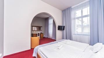 A hotel room with a bed, a desk with a chair, a television, and a window with curtains.