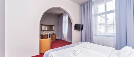 Une chambre d’hôtel comprenant un lit, un bureau avec une chaise, une télévision et une fenêtre avec des rideaux.