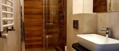 Une salle de bain moderne avec une douche à parois de verre, des toilettes blanches et un lavabo sur un plan de travail noir.