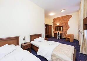 Habitación de hotel con dos camas, una pared decorativa de ladrillo, un escritorio con silla y un espejo grande.