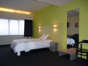 Ein Hotelzimmer mit einem Bett, Nachttischen, einem Sessel, einem Schreibtisch und einem Spiegel.