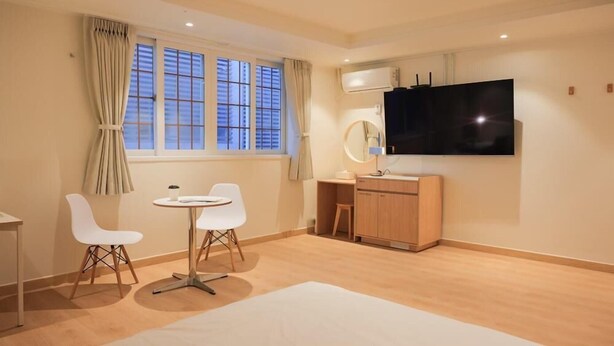 A room with a TV, a desk, two chairs, a window with curtains, and a radiator. - Ace Hotel By Cozy Daejeon Yuseong Branch (Daejeon)