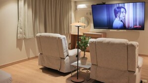 A living room with two beige armchairs, a small table with a plant, a floor lamp, and a flat-screen TV mounted on the wall. - Ace Hotel By Cozy Daejeon Yuseong Branch (Daejeon)