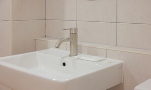 Une salle de bain avec un lavabo blanc, un robinet moderne et un miroir au-dessus.