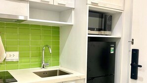 Une cuisine de taille réduite avec des meubles blancs, un crédence en carreaux verts, un réfrigérateur noir et un évier en acier inoxydable.