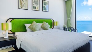 Une chambre d’hôtel avec un lit, une tête de lit verte, du linge de lit blanc et une vue sur la mer.
