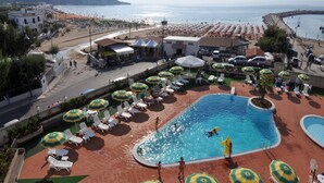A pool area with sun loungers and umbrellas, a beach in the background, and a view of the sea. - Morcavallo Hotel & Wellness (Peschici)