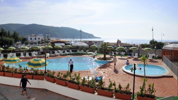 A pool area with multiple sun loungers and umbrellas, surrounded by potted plants and a view of the sea. - Morcavallo Hotel & Wellness (Peschici)