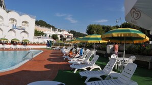 A poolside area with lounge chairs and umbrellas, a swimming pool, and a building with arches and a sign. - Morcavallo Hotel & Wellness (Peschici)