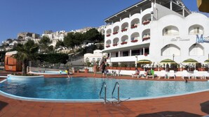 A swimming pool area with a building in the background, a palm tree, and a view of a hillside. - Morcavallo Hotel & Wellness (Peschici)