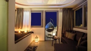 A modern living room with a sofa, a hanging chair, a small table with candles, and a view of the night sky through a window. - Tataki Family Hotel (Santorini)