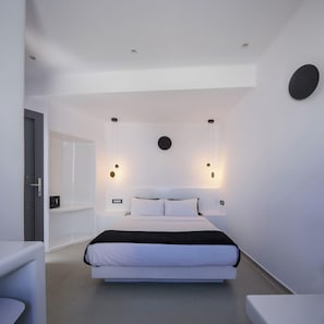 A modern bedroom with a bed, bedside tables, and wall-mounted lighting. - Tataki Family Hotel (Santorini)